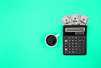 Coffee cup stands next to a calculator with banknotes in it