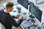 Ein Mann sieht vor Bildschirmen und programmiert.