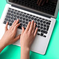 Hand types on a laptop standing on a green table.