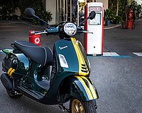 green Vespa with yellow stripe in front of petrol pump