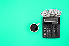 Cup of coffee, calculator and banknotes on green background.