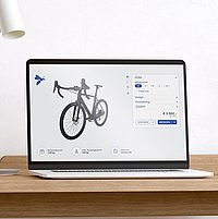 Laptop auf einem Holztisch. Am Bildschirm sieht man einen Fahrrad Konfigurator.